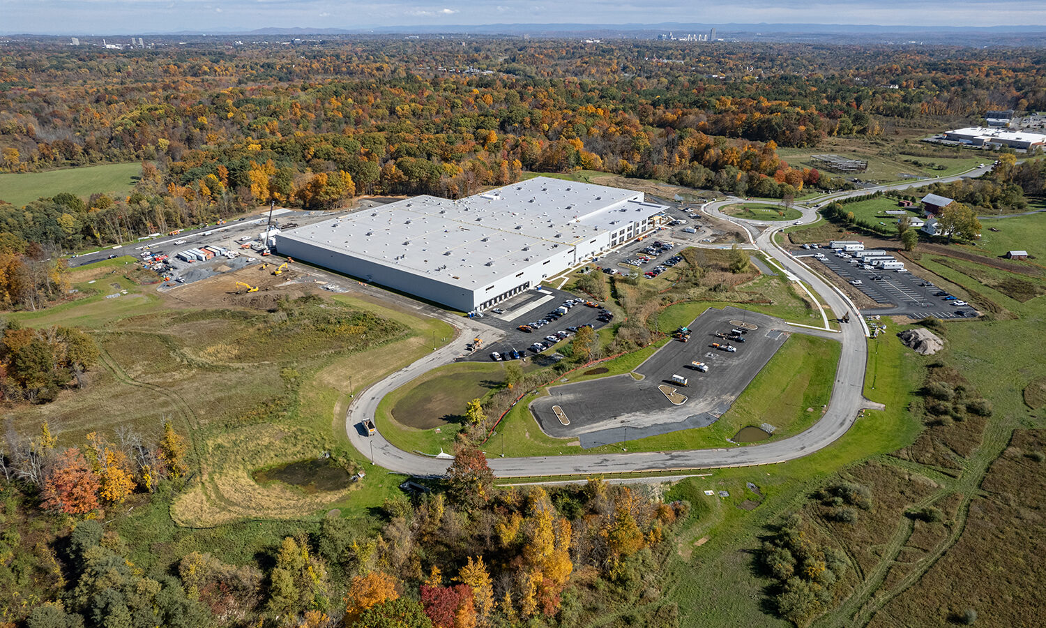 Aerial view: warehouse and parking amid autumn trees and fields.