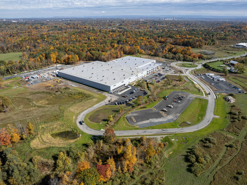 Aerial view: warehouse and parking amid autumn trees and fields.