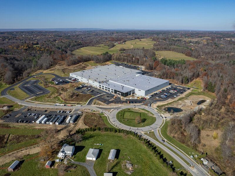Aerial view of warehouse with parking, roads, and surrounding fields.
