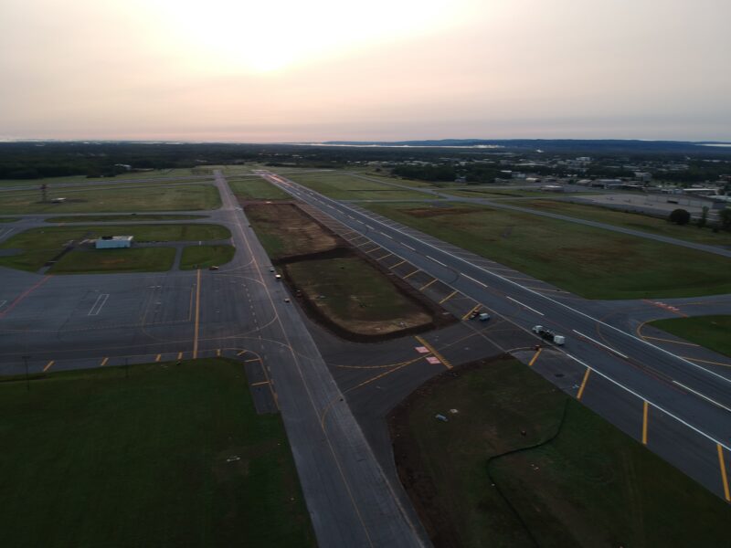 Aerial sunset view of runway construction with vehicles visible.