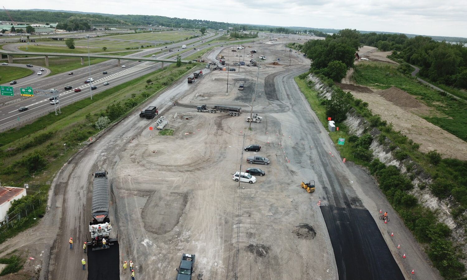 Aerial view: highway construction, machinery, vehicles, workers under clouds.