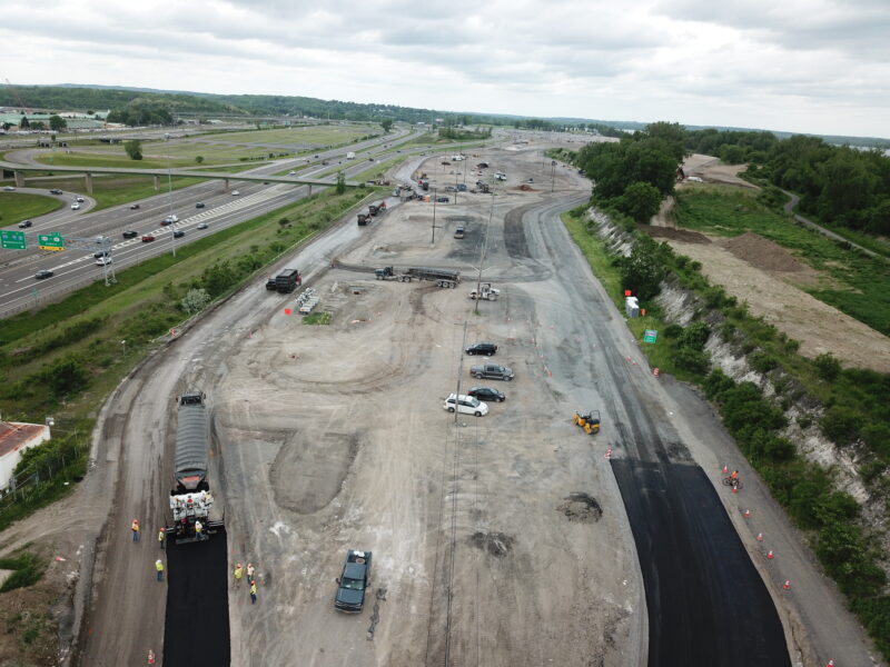 Aerial view: highway construction, machinery, vehicles, workers under clouds.