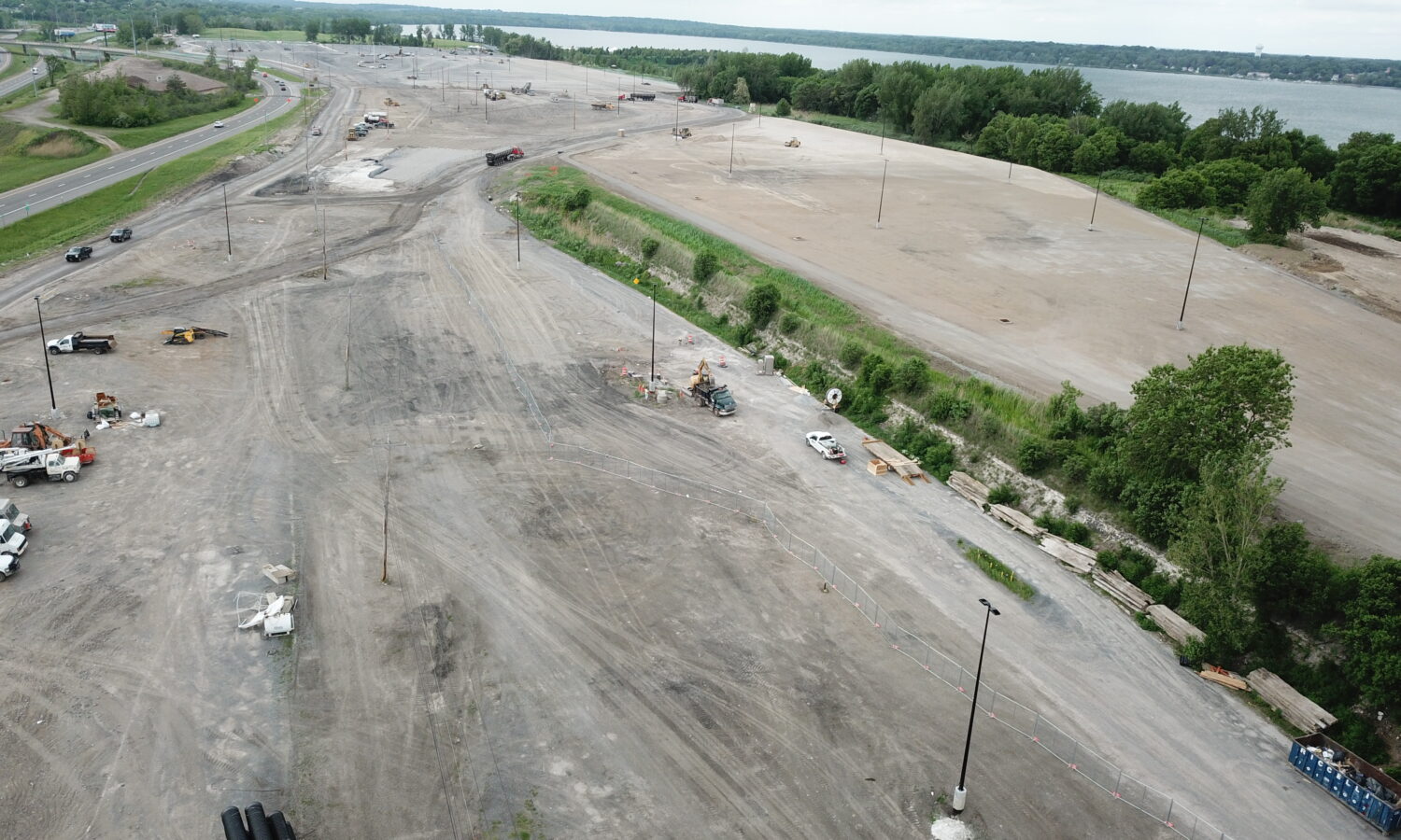 Aerial of construction site, vehicles, water, greenery, and roads.