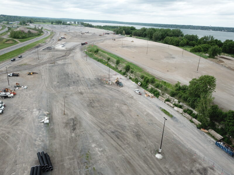 Aerial of construction site, vehicles, water, greenery, and roads.