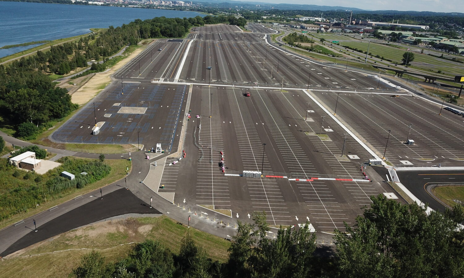 Sparse parking lot by water, few cars, greenery around.