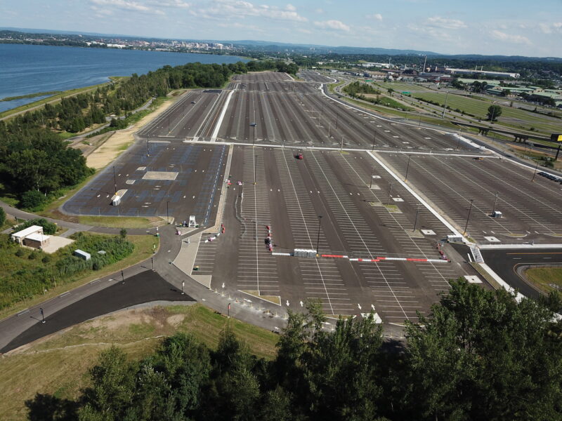 Sparse parking lot by water, few cars, greenery around.