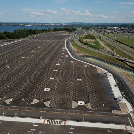 Empty parking lot by water and highway, under cloudy sky.