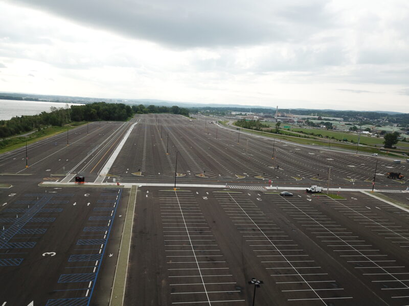 Empty parking lot with marked spaces, few light poles, cloudy.