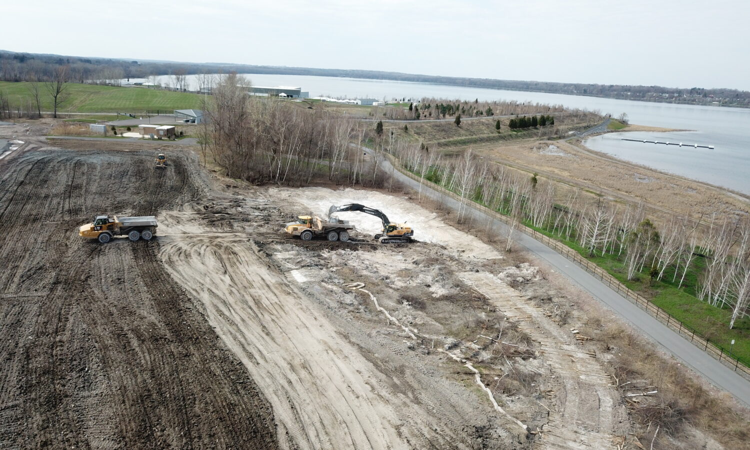 Aerial view: construction vehicles clear land by water and road.