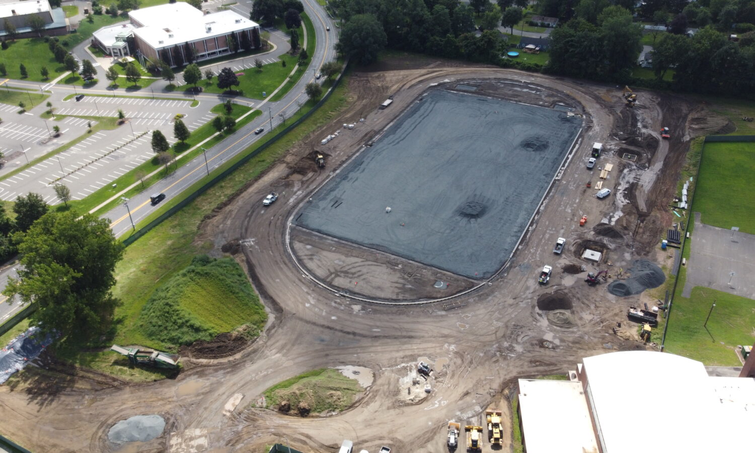 Aerial view: large gravel construction site with vehicles around and nearby buildings