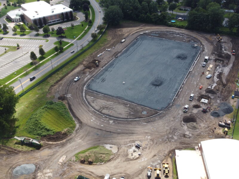 Aerial view: large gravel construction site with vehicles around and nearby buildings