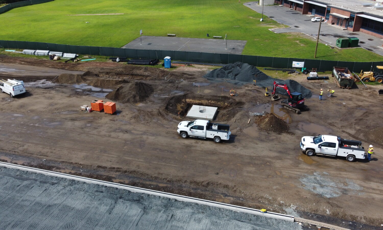 Construction site with trucks, equipment, dirt piles, and workers.