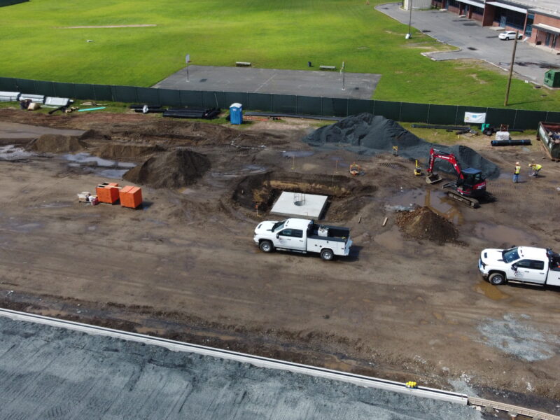 Construction site with trucks, equipment, dirt piles, and workers.