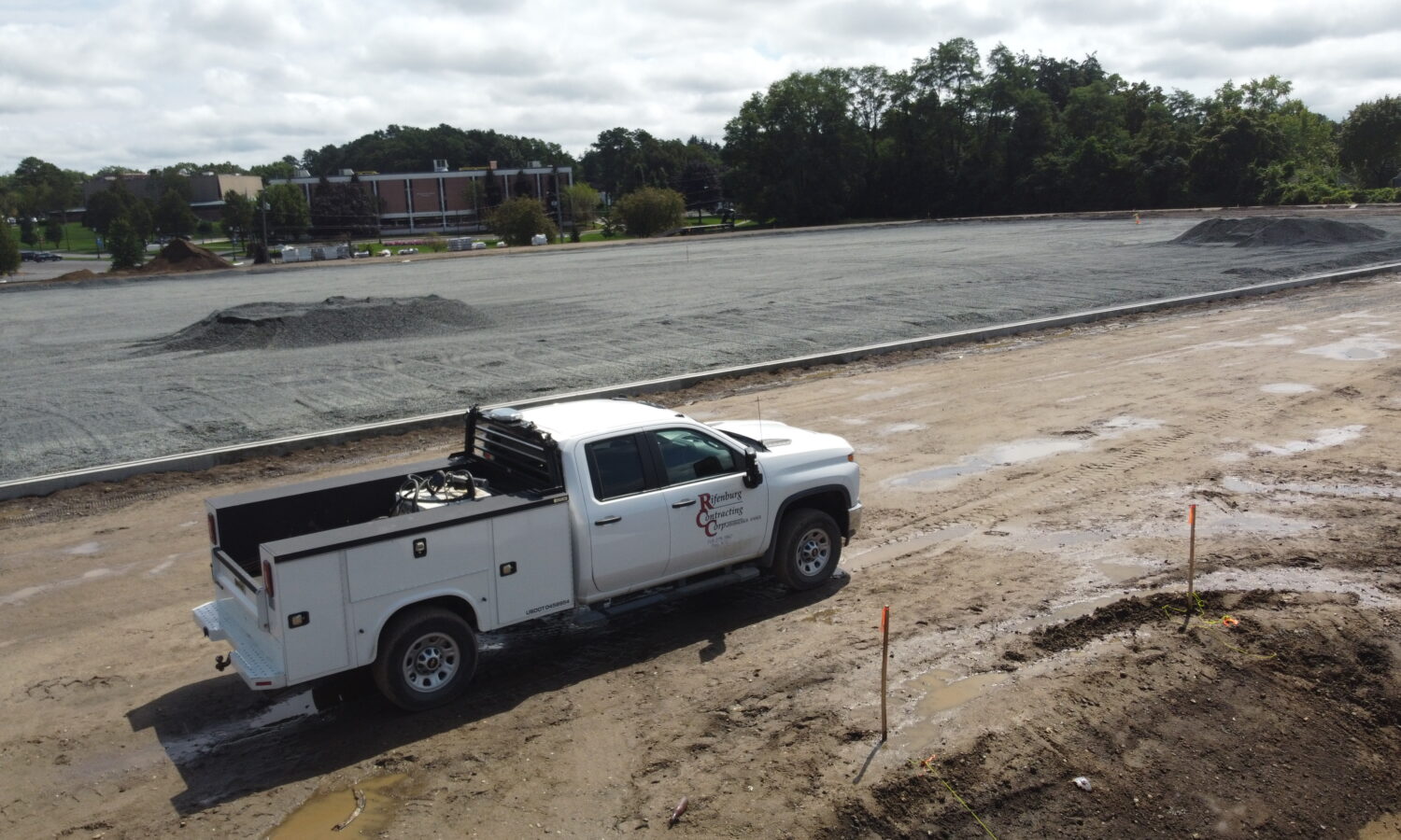 White utility truck parked on muddy dirt road next to gravel construction site.