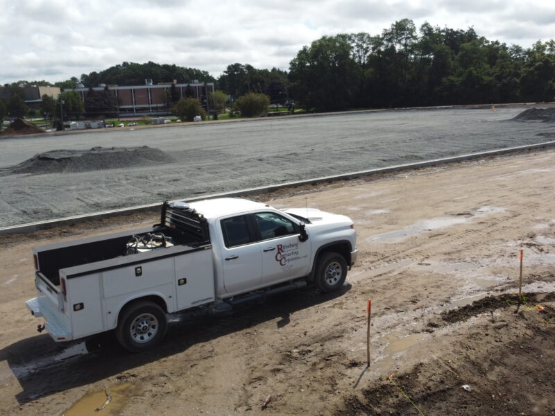 White utility truck parked on muddy dirt road next to gravel construction site.