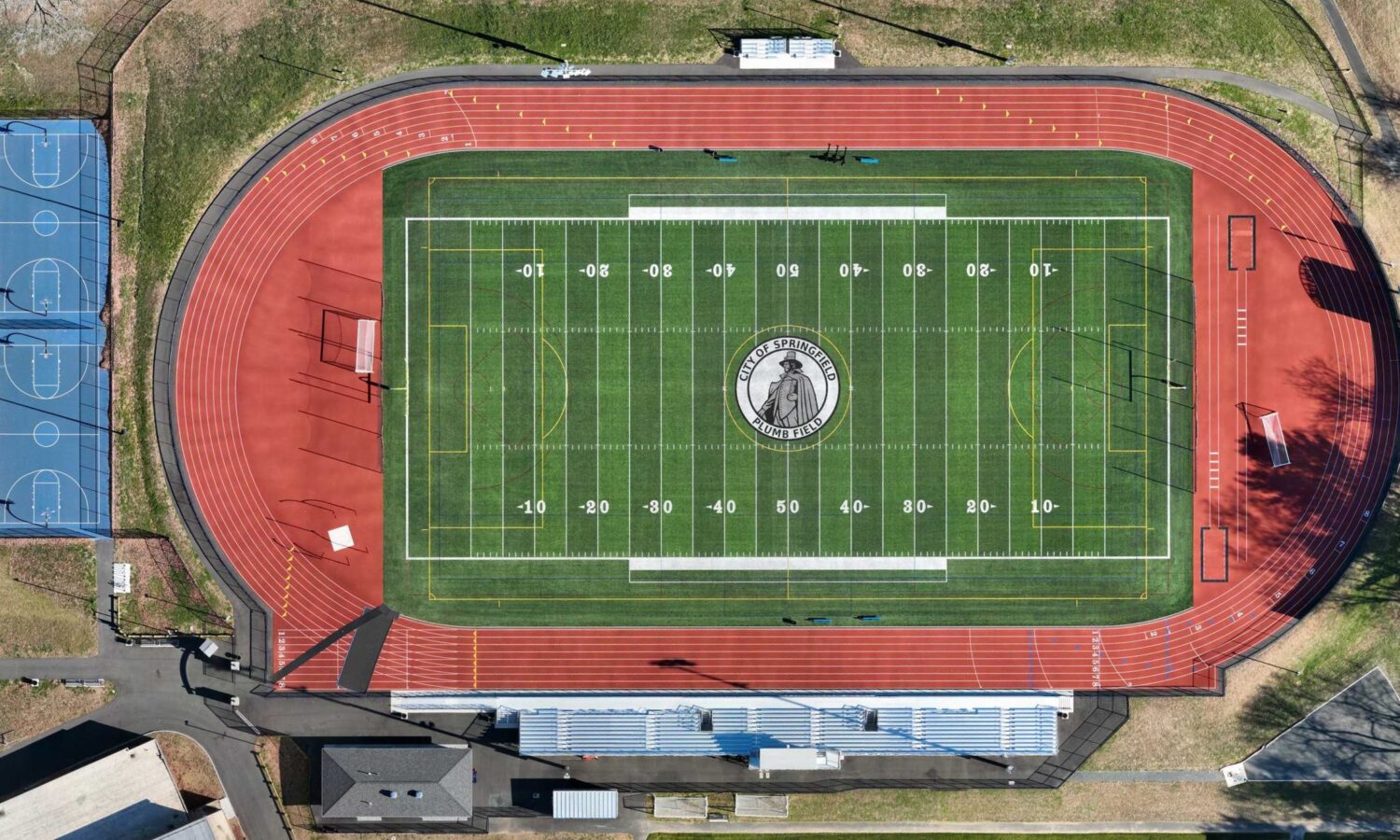 Aerial view: football field with mascot, track, bleachers, courts.