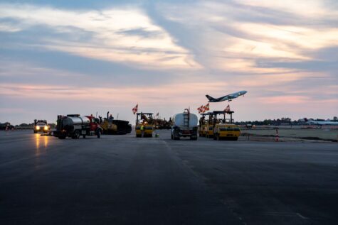 Two large dump trucks drive on a dirt construction site.