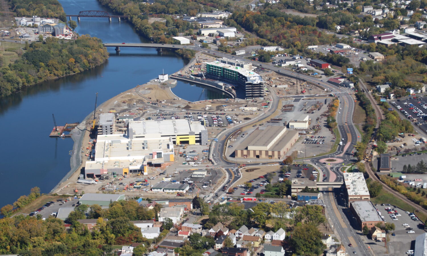 Aerial view: riverside construction, buildings, bridge, trees nearby.