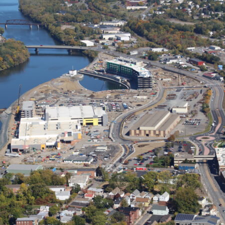 Aerial view: riverside construction, buildings, bridge, trees nearby.