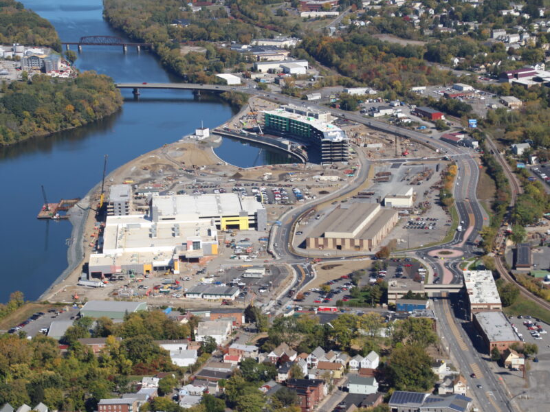Aerial view: riverside construction, buildings, bridge, trees nearby.