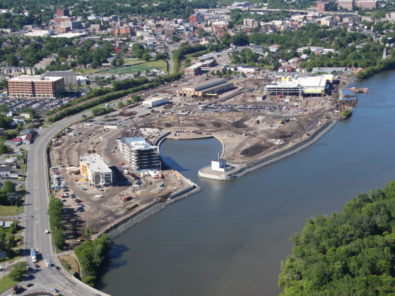 Aerial of waterfront construction, bridge, urban area, and greenery.