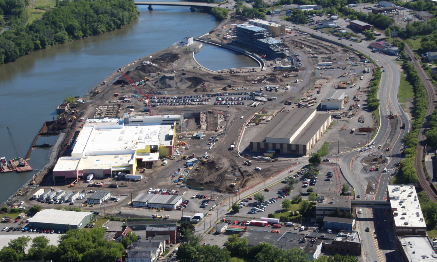 Aerial view of riverside construction site, river, and bridge.