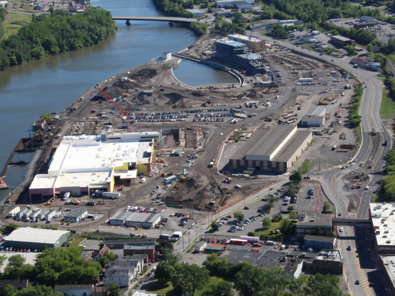 Aerial view of riverside construction site, river, and bridge.