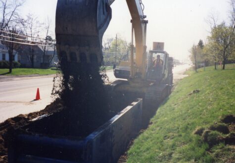 Two large dump trucks drive on a dirt construction site.