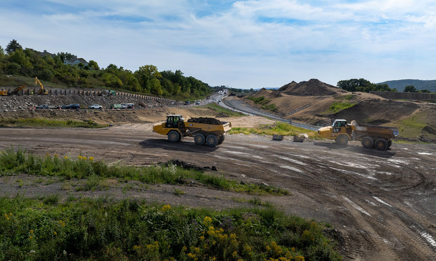 Two large dump trucks drive on a dirt construction site.