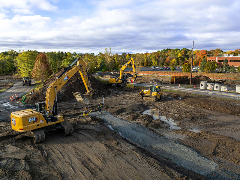 Three excavators and workers at busy construction site.
