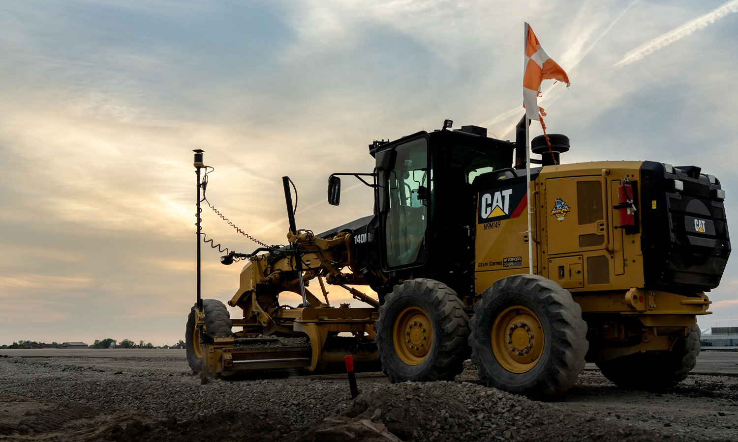Yellow Caterpillar grader parked on gravel at sunset